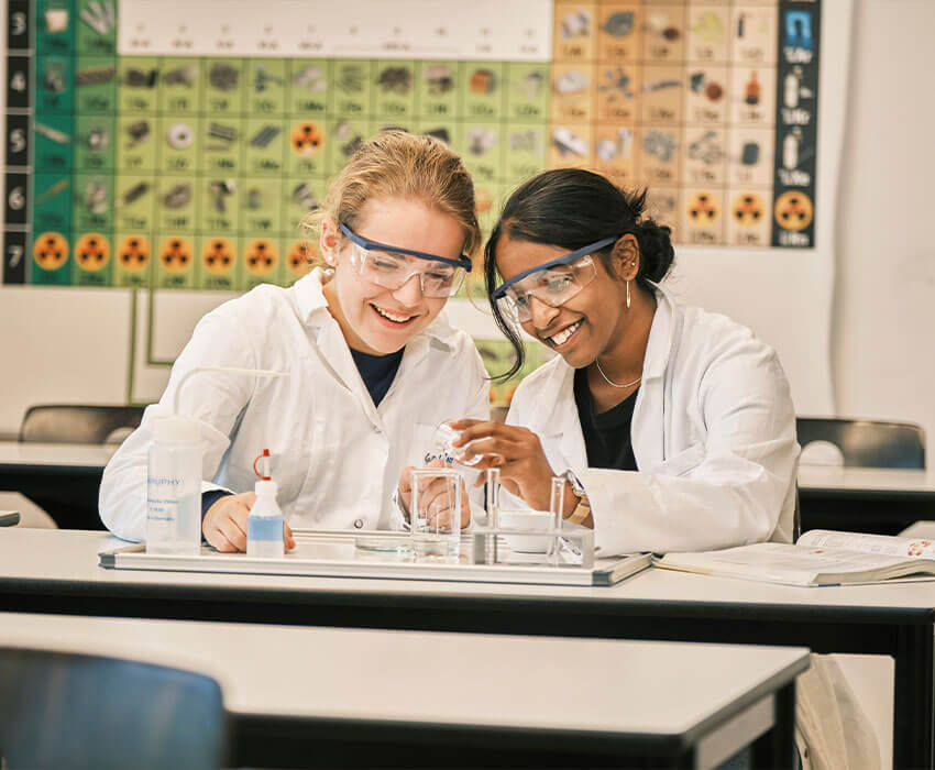 Zwei Schülerinnen sitzen im Chemieraum und arbeiten an einem gemeinsamen Experiment