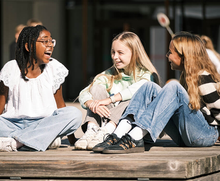 Drei Mädchen sitzen auf einer Holzbank und lachen gemeinsam