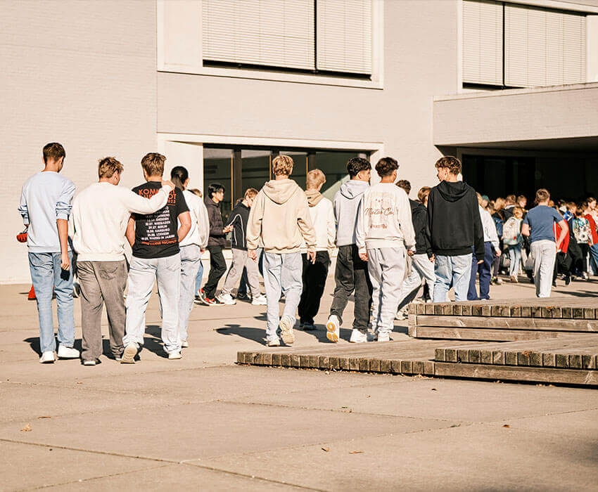 Eine Schülerin steht im Vordergrund und lächelt in die Kamera dahinter sind zwei die sich unterhalten und links davon nochmal zwei