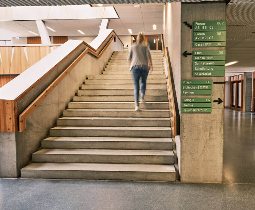 Eine Mutter mit ihrer Tochter lasse sich von einem Lehrer etwas im Schulflur auf einem Clippboard erklären